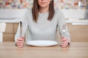 Displeased young woman sitting at the empty plate. Shallow depth of field, focus on foreground