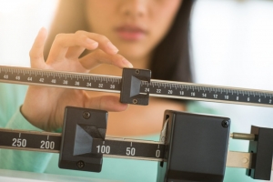 Midsection of mid adult Asian woman adjusting balance weight scale